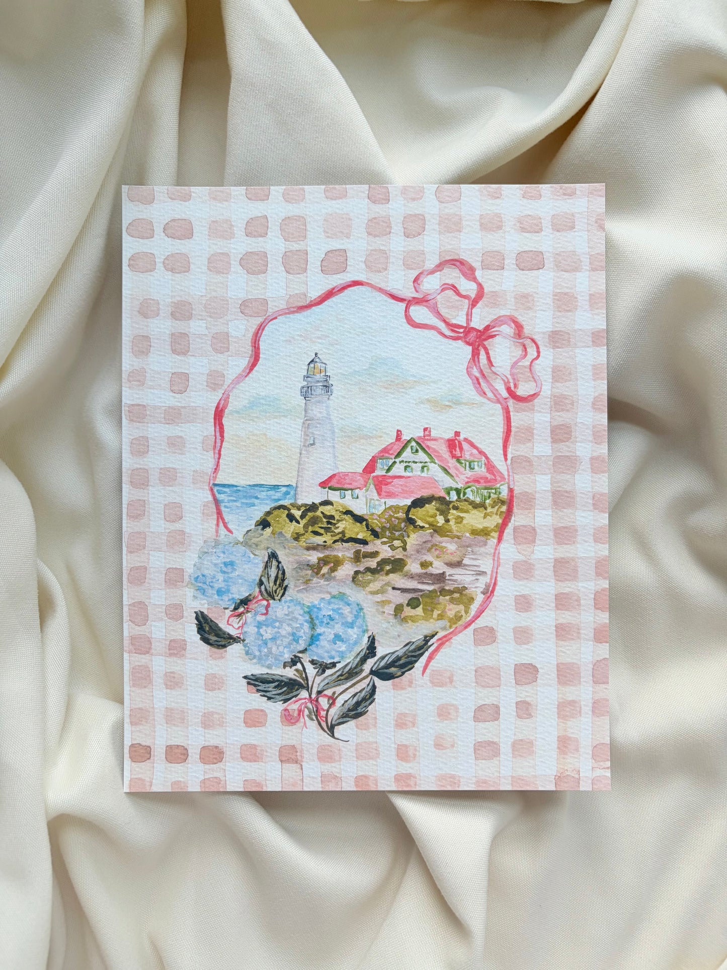 Art Print with a lighthouse illustration on a checkered background, with ribbon and hydrangeas bordering it, placed on a textured fabric surface.